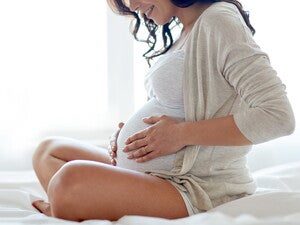 אישה הרה יושבת על הרצפה ומניחה את ידיה על בטנה