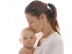 אמא צעירה מנשקת את תינוקה בראשון