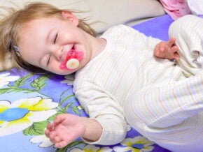 תינוקת שוכבת על גבה עם מוצץ בפיה