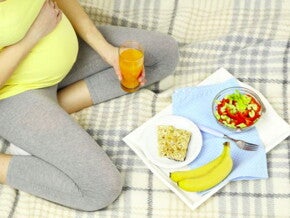 אישה הרה יושבת על שמיכת פיקניק בדשא ומולה ארוחת בוקר