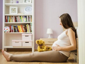 הריונית יושבת על הרצפה עם בובה על רגלייה