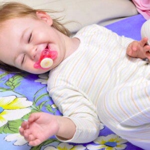 תינוקת שוכבת על גבה עם מוצץ בפיה