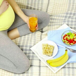 אישה הרה יושבת על שמיכת פיקניק בדשא ומולה ארוחת בוקר