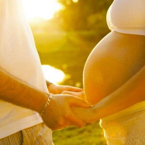 אישה הרה ובן זוגה אוחזים ידיים בשקיעה כשביניהם מפרידה בטן הריונית