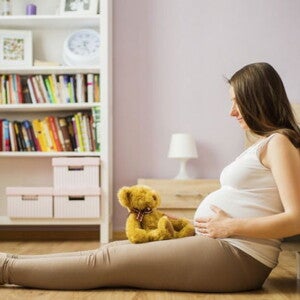 הריונית יושבת על הרצפה עם בובה על רגלייה