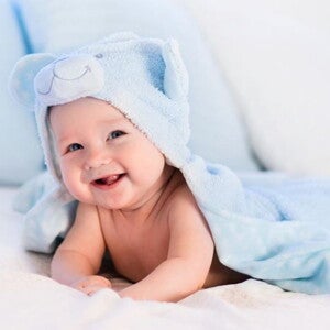 תינוק עטוף מגבת כחולה מחייך ללא שיניים