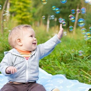 תינוק יושב ומרים ידו אל בועות סבון