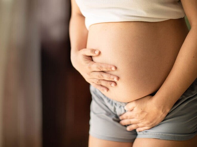 אישה הרה עם בטן חשופה מניחה את ידה האחת על ביטנה ואת ידה השניה על המפשעה