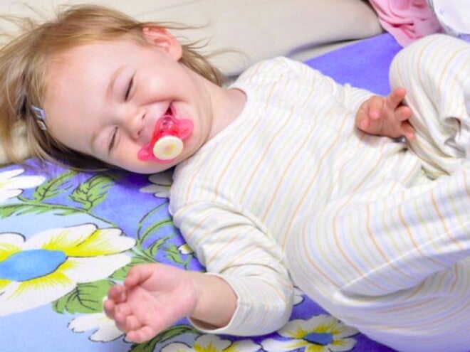 תינוקת שוכבת על גבה עם מוצץ בפיה