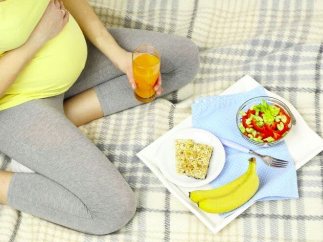 אישה הרה יושבת על שמיכת פיקניק בדשא ומולה ארוחת בוקר