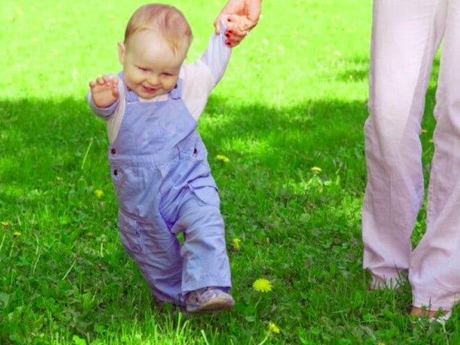 פעוט הולך על הדשא ואוחז בידה של אימו