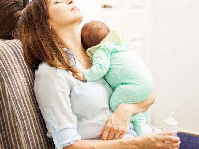 אמא מנמנמת בישיבה בעודה מחזיקה את ביתה