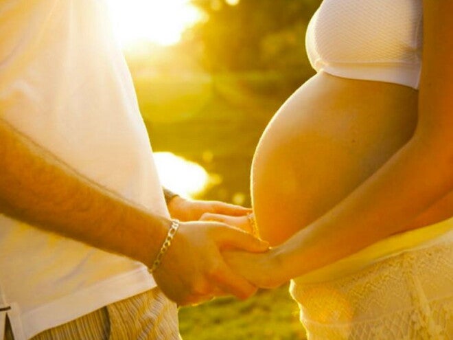 אישה הרה ובן זוגה אוחזים ידיים בשקיעה כשביניהם מפרידה בטן הריונית