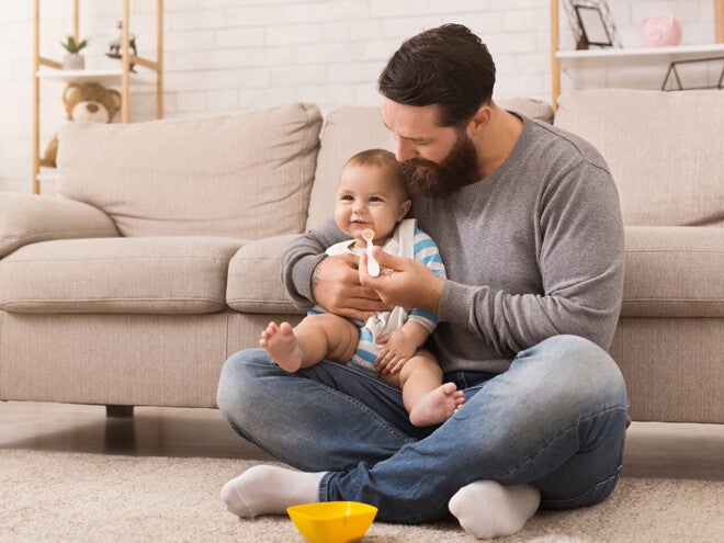 אב ומאכיל את בנו על שטיח בסלון
