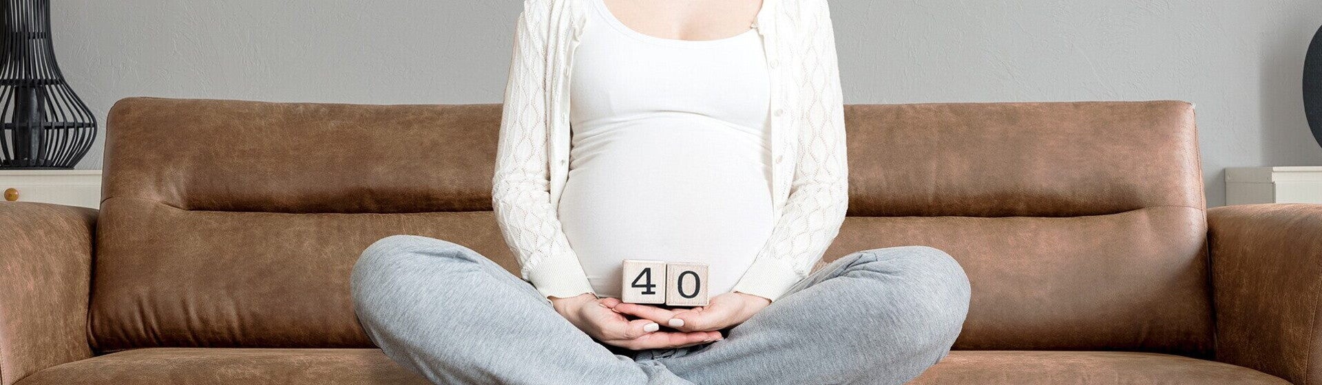 אישה הרה יושבת על הספה ומחזיקה שתי קוביות שיחד מציגות את המספר 40