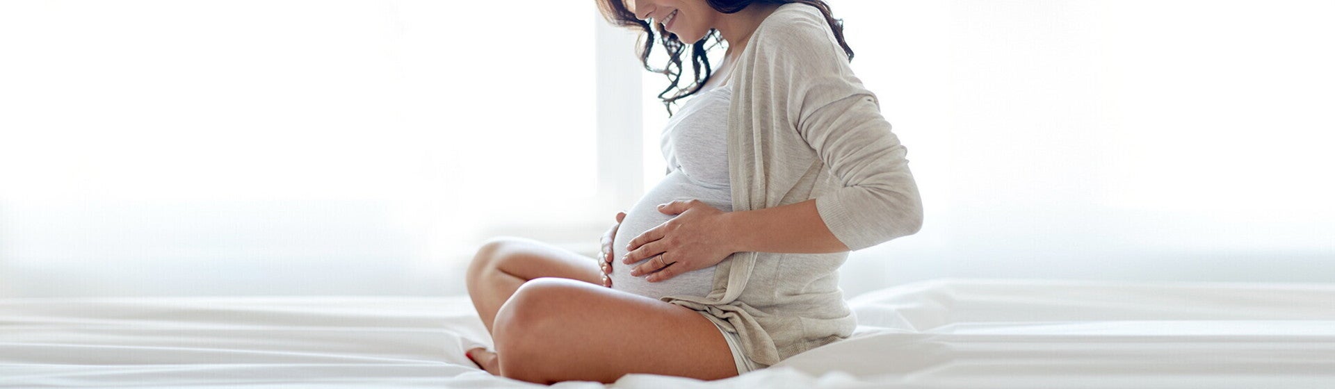 אישה הרה יושבת בישיבה מזרחית כשידיה על בטנה