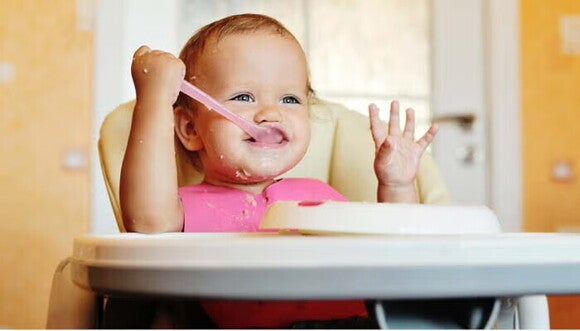 תינוק יושב בכיסא אוכל ואוכל עם כפית