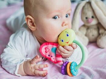 תינוק שוכב על בטנו ומכניס לפיו צעצוע