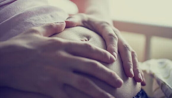 אמא בהריון מסמנת לב עם הידיים על הבטן