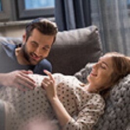 אישה הרה שוכבת על גבה ובן זוגה מלטף בשמחה את הבטן שלה