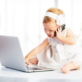 פעוטה מדברת בטלפון ומשחקת במחשב הנייד